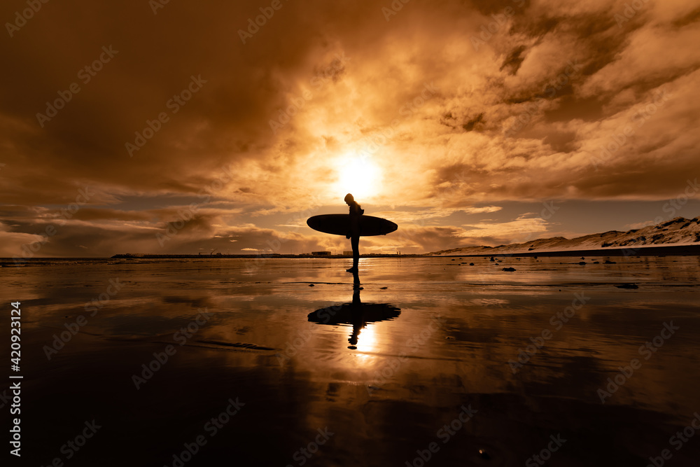 Silhouette of a woman carrying a surfboard walking across a beach with a sunset in the background. Silhouette of a woman carrying a surfboard walking across a beach with a sunset in the background.