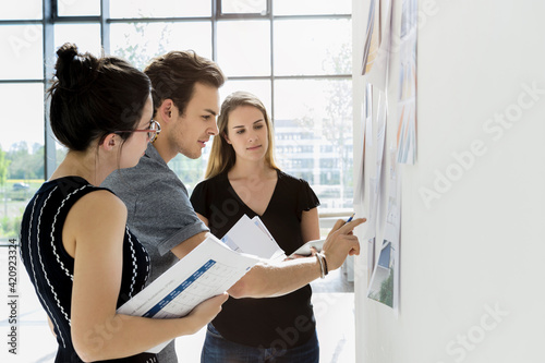 Three young architects standing at whiteboard, discussing design ideas. photo