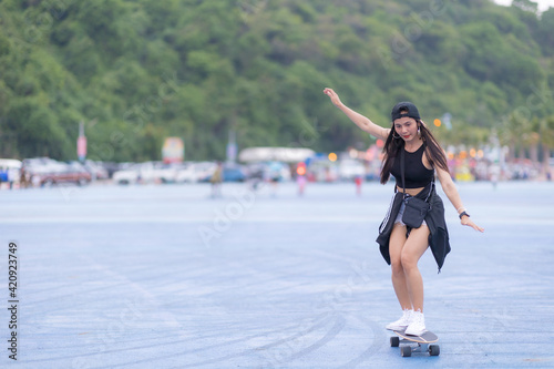 Asian woman playing surf skate or skates board outdoors on beautiful summer day. Happy young women play surf skate at park on morning time in the park.