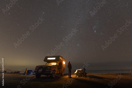 Person standing next to camper-van parked near Jordan River, British Columbia, Canada at night. 