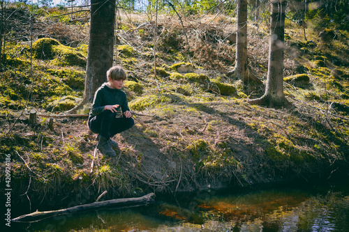 Boy kneeling on riverbank in a forest in Vasterbottens Lan, Sweden. photo