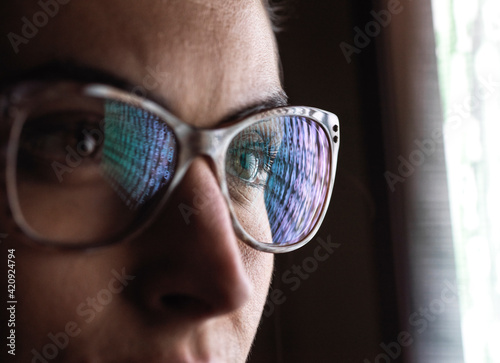 Female data analyst looking at data on screen, reflection in glasses.