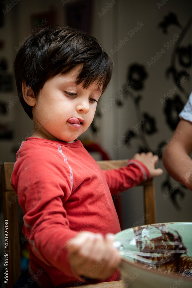 Young boy with black hair sitting at a kitchen table, baking chocolate cake. Young boy with black hair sitting at a kitchen table, baking chocolate cake.