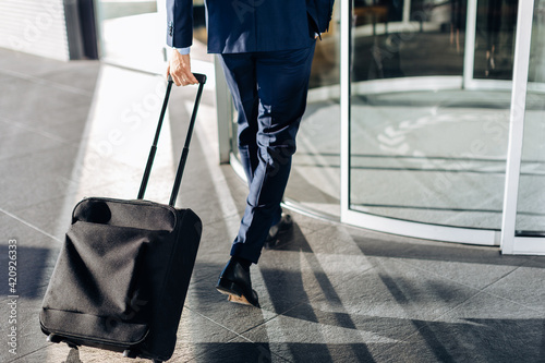 Businessman with wheeled luggage entering revolving doors of building photo