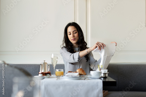 Young woman preparing napkin whilst having champagne breakfast at  boutique hotel in Italy