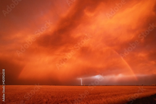 A dust storm with vivid orange sky and rainbow, and cloud-to-ground lightning strike.  photo