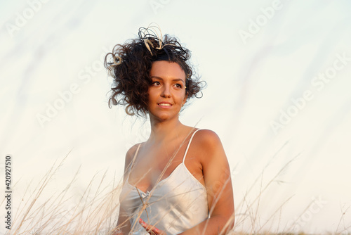 Portrait of beautiful woman with brown curly hair hair, wearing white silk chemise.