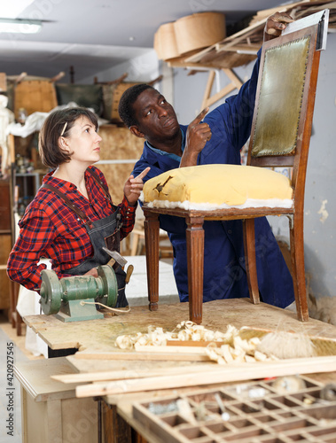 Portrait of male and female restorers working with vintage wooden armchair in workshop