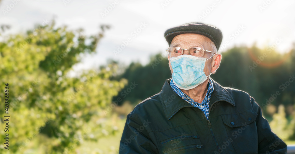 Adult man wearing cap and medical mask sitting on bench in park. Adult man wearing cap and medical mask sitting on bench in park.