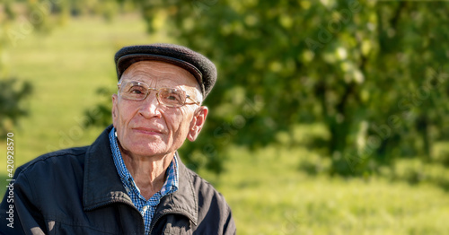 Fototapeta Naklejka Na Ścianę i Meble -  Older man wearing cap and eyeglasses looks at camera stands outdoor