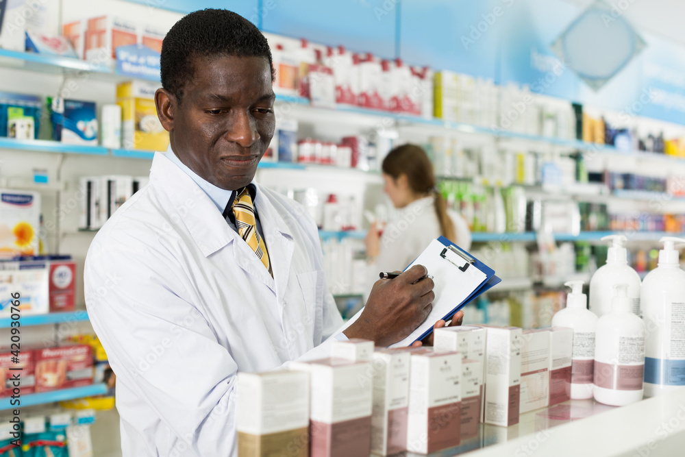 African American man pharmacy specialist making notes on clipboard during inventory in pharmacy
