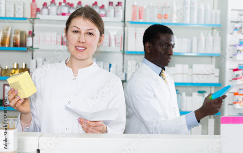 Woman pharmaceutist counseling about medicines in pharmacy, man pharmacist on background.