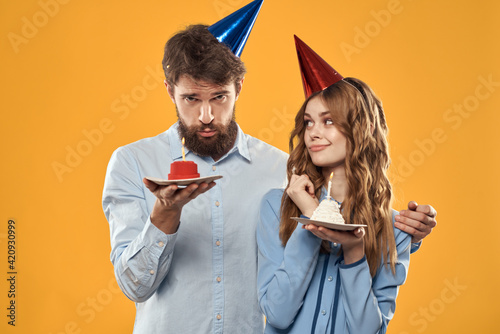 Man and woman with a birthday cake and in caps on a yellow background party fun yellow background