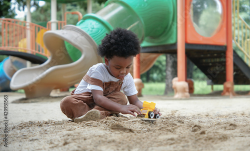African little boy with afro hair enjoy playing sand on playground outdoors. Adorable kid having fun with sand and toys loader in the park on a sunny day