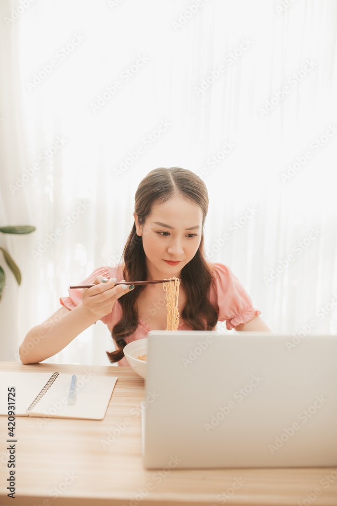 Female employee holding chopsticks eating instant noodle at workplace in home office Female employee holding chopsticks eating instant noodle at workplace in home office