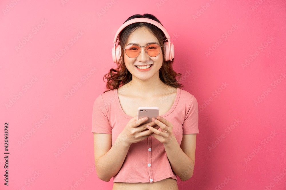 Young asian girl wearing headphones and using the phone on pink background Young asian girl wearing headphones and using the phone on pink background