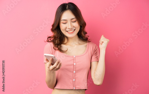 Young asian girl using the phone on pink background
