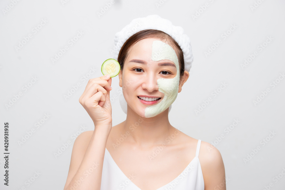 Attractive young Asian woman with clay mask and holding fruit piece isolated over white background. Beauty concept. Attractive young Asian woman with clay mask and holding fruit piece isolated over white background. Beauty concept.