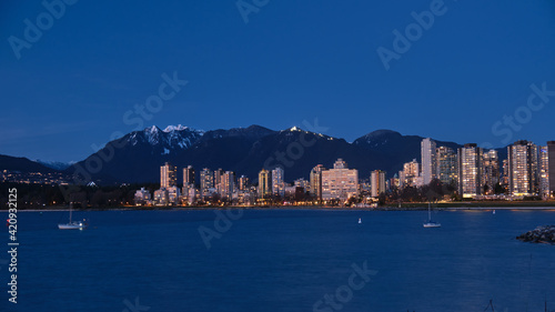 Highrise buildings by ocean and mountains at dusk. West side Vancouver and grouse mountain from Kitcilano Beach. British Columbia. Canada 