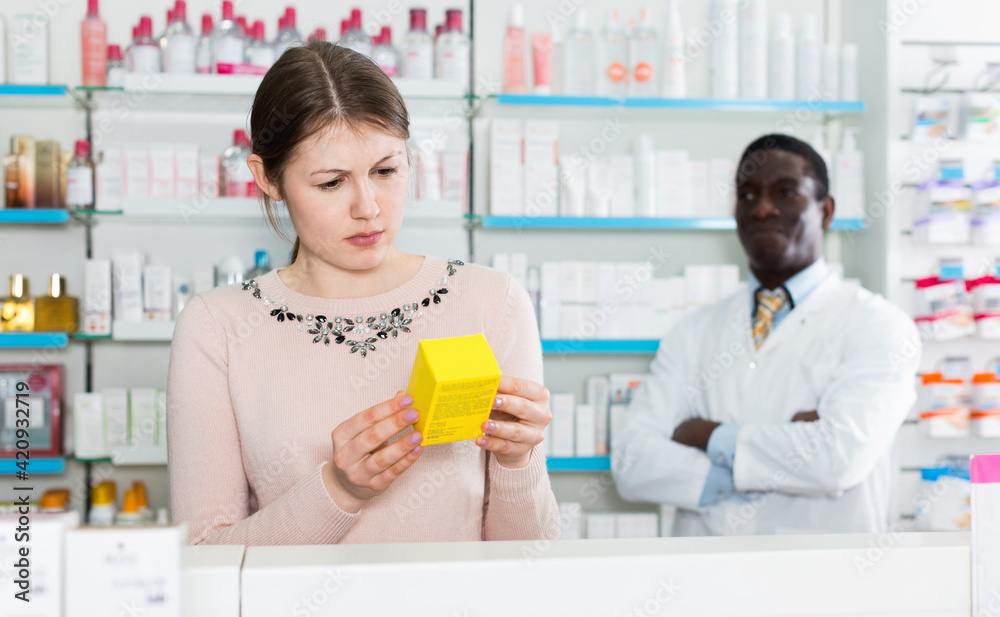 Pensive serious pleasant young woman choosing medicines in modern pharmacy
