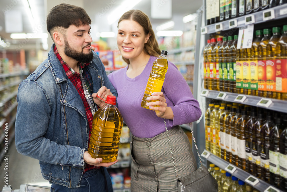 Loving young couple shopping in grocery shop, choosing bottled vegetable oils