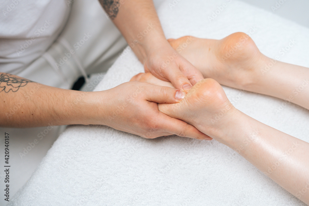 Male masseur massaging feet to young relaxing woman lying on massage table, close-up. Professional physiotherapist with strong hands performing foot massage. Concept of massage spa treatments Male masseur massaging feet to young relaxing woman lying on massage table, close-up. Professional physiotherapist with strong hands performing foot massage. Concept of massage spa treatments
