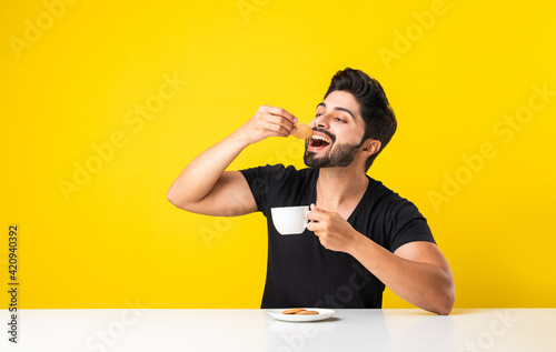 Indian young man eating round biscuit with tea or coffee photo