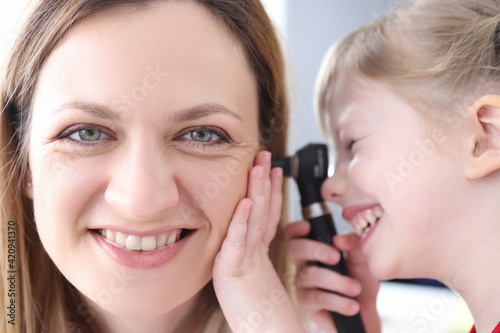 Little girl looking at ear of woman doctor with otoscope
