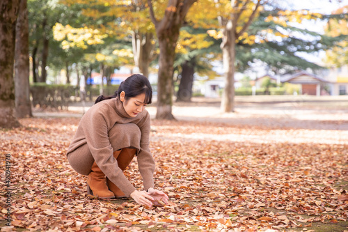 秋の公園の落ち葉で遊ぶ女性 