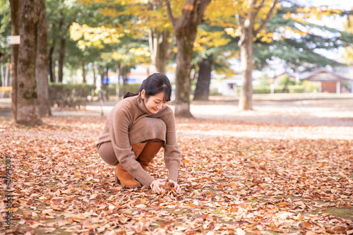 秋の公園の落ち葉で遊ぶ女性 