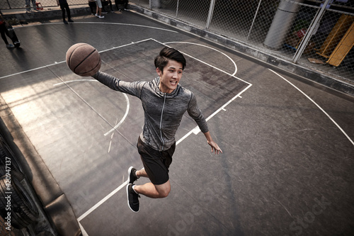 young asian male basketball player attempting a dunk