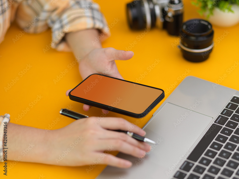 Fototapeta premium Female photographer working smartphone and laptop on stylish workspace in studio