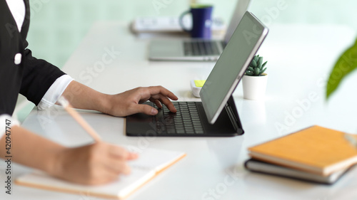 Female hand writing on notebook and typing on tablet keyboard on office desk