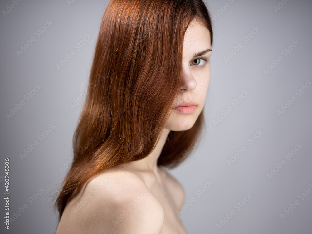 Naklejka premium Portrait of a luxurious woman with red hair and bare shoulders on a gray background