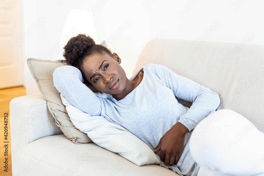 Woman lying on sofa looking sick in the living room. Beautiful young woman lying on bed and holding hands on her stomach. Woman having painful stomachache on bed, Menstrual period