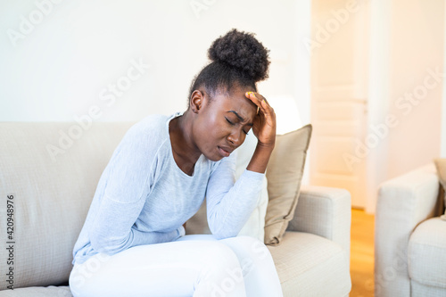 African American Woman in painful expression holding hands against belly suffering menstrual period pain, lying sad on home bed, having tummy cramp in female health concept © Graphicroyalty