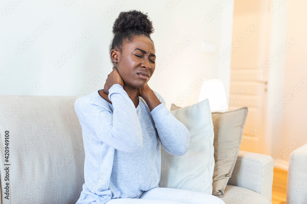 Young Black woman feeling pain in neck , sitting sad on home bed. Tired ...