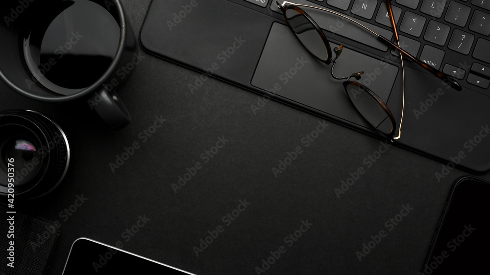 Dark creative flat lay workspace with eyeglasses, coffee cup, tablet keyboard and copy space