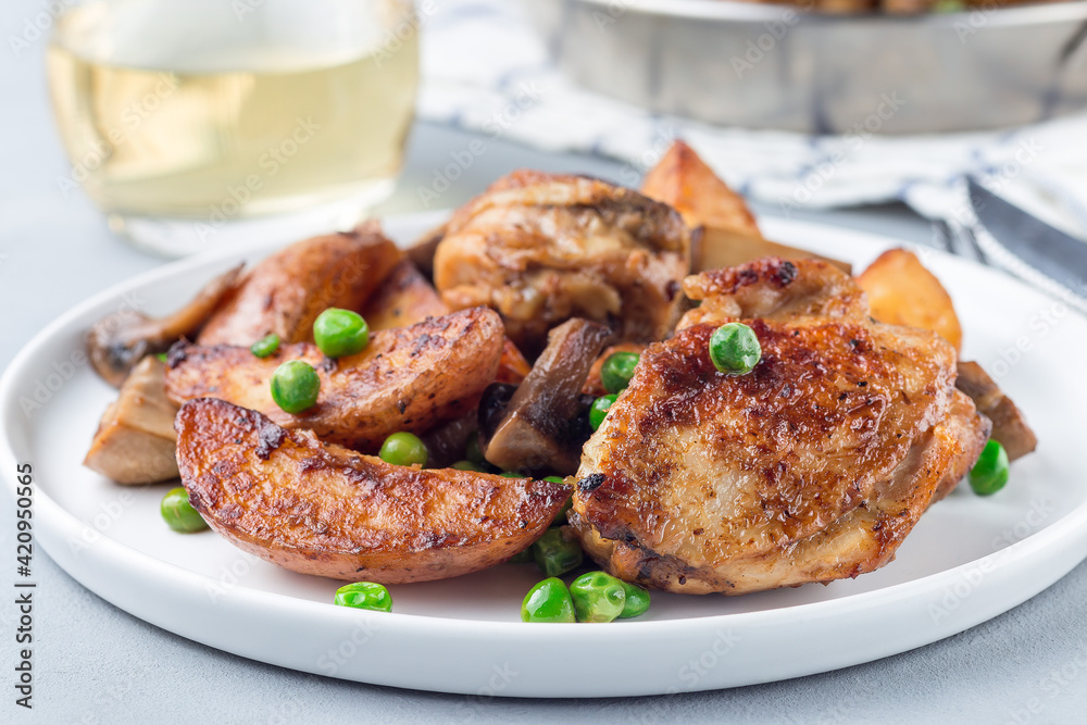 Chicken with potatoes, mushrooms and green peas, on a white plate and in metal pot, horizontal Chicken with potatoes, mushrooms and green peas, on a white plate and in metal pot, horizontal
