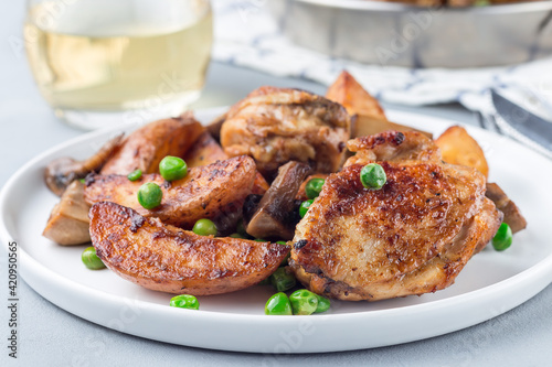 Chicken with potatoes, mushrooms and green peas, on a white plate and in metal pot, horizontal