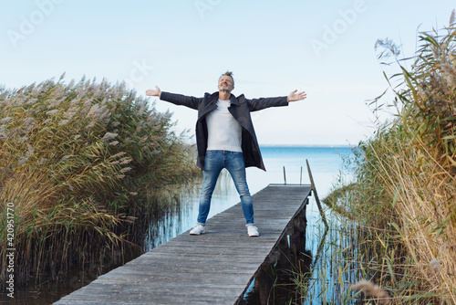 Senior man rejoicing with outstretched arms on a wooden jetty