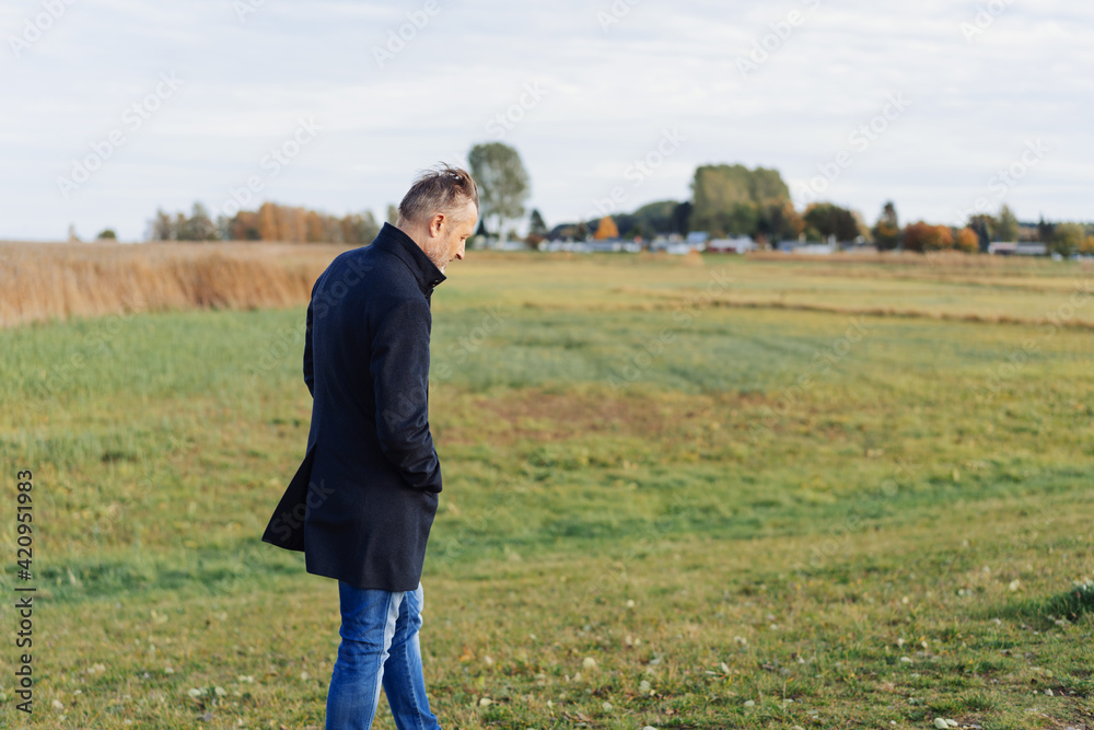 Lonely middle-aged man walking across coastal grassland