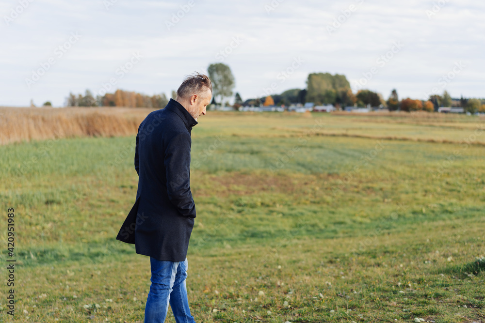 Lonely middle-aged man walking across coastal grassland Lonely middle-aged man walking across coastal grassland