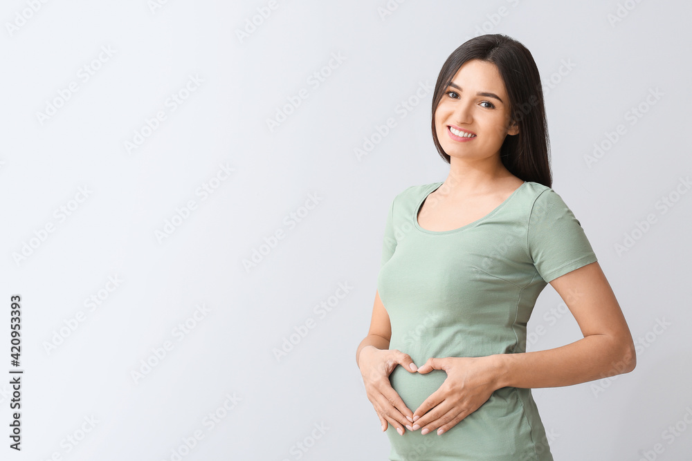 Beautiful pregnant woman making heart with her hands on light background Beautiful pregnant woman making heart with her hands on light background