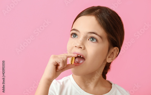 Little girl taking fish oil pill on color background
