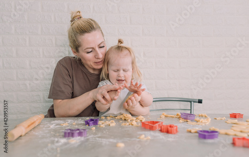 happy young mother and her little daughter together prepare delicious cookies sitting at the table in the home kitchen