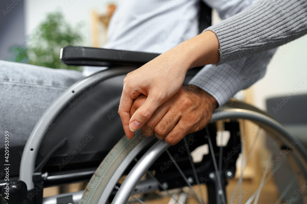 Close up of female touching hand of disabled man in wheelchair for support Close up of female touching hand of disabled man in wheelchair for support