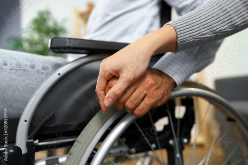 Close up of female touching hand of disabled man in wheelchair for support