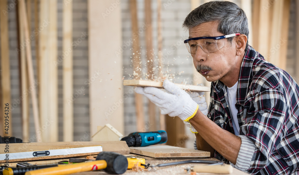 Elderly craftsman blowing wooden dust from board Elderly craftsman blowing wooden dust from board