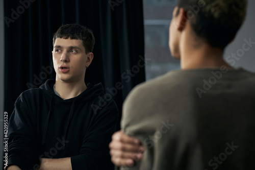 Staged photo illustrates problems and conflicts in gay couple relationships. Moment of showdown: young black-haired man is standing in front of his partner and looking away.